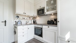 Een moderne keuken met witte kasten, een inbouwoven, een magnetron en een koffiezetapparaat.