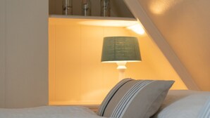 Un dormitorio con una cama, una lámpara de noche y una estantería con botellas.