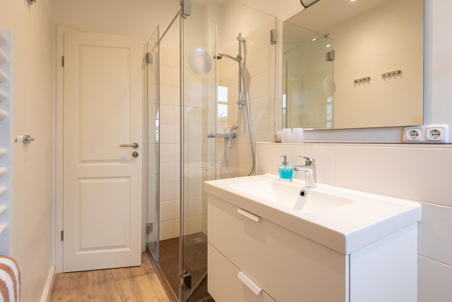 A modern bathroom with a glass-enclosed shower, a white sink with a soap dispenser, and a mirror above the sink.
