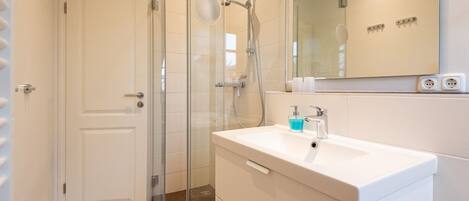 A modern bathroom with a glass-enclosed shower, a white sink with a soap dispenser, and a mirror above the sink.