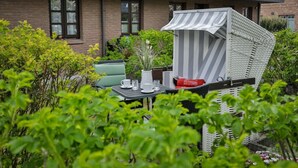 Un patio con zona de estar al aire libre a rayas, una mesa con tazas y un florero, y una casa de ladrillo al fondo.