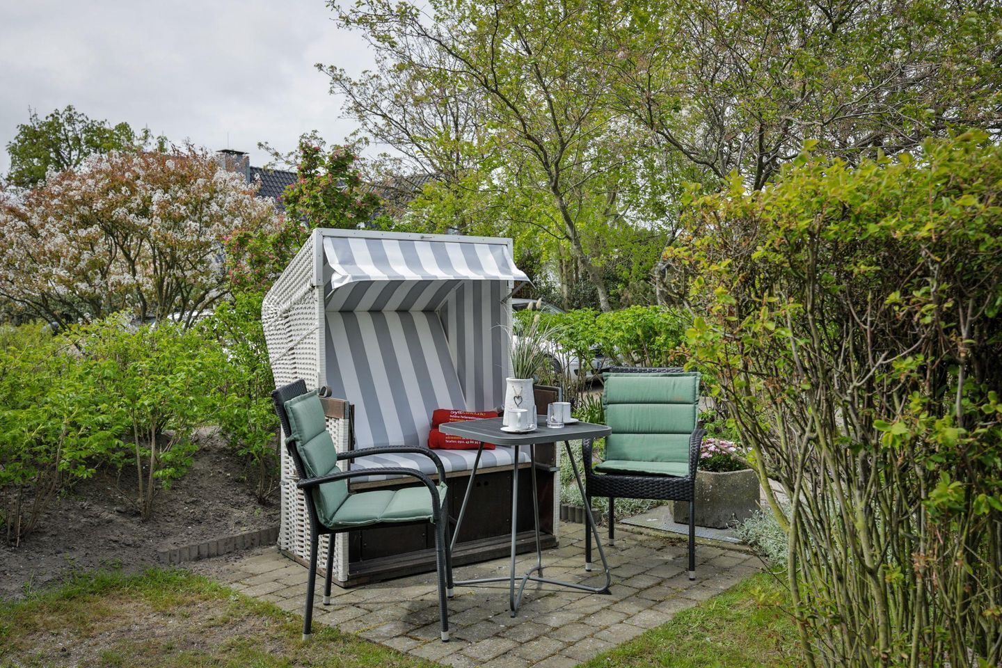 A patio with a striped canopy, two chairs, a table, and a small shed.
