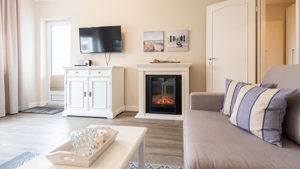 A living room with a fireplace, a television, and a sofa. - Haus Südstrand Whg. 174 - Haus Südstrand, Gemütliche 2-zimmerwohnung auf ca. 38 m² für bis zu 4 (Sylt)