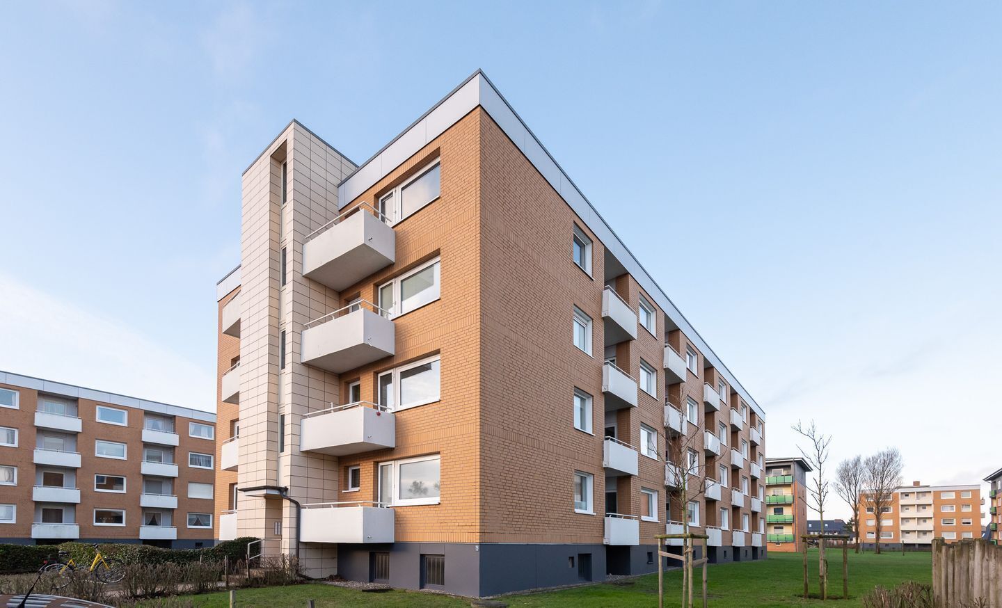 Ein mehrgeschossiges Wohngebäude mit Balkonen, einer flachen Dachkonstruktion und einer Ziegel-Fassade.