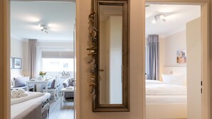 A hotel room with a bed, a sitting area with a table and chairs, and a large mirror on the wall. - Haus Südstrand Whg. 174 - Haus Südstrand, Gemütliche 2-zimmerwohnung auf ca. 38 m² für bis zu 4 (Sylt)