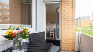 A balcony with a wicker chair, a glass table, and a vase with flowers. - Haus Südstrand Whg. 174 - Haus Südstrand, Gemütliche 2-zimmerwohnung auf ca. 38 m² für bis zu 4 (Sylt)