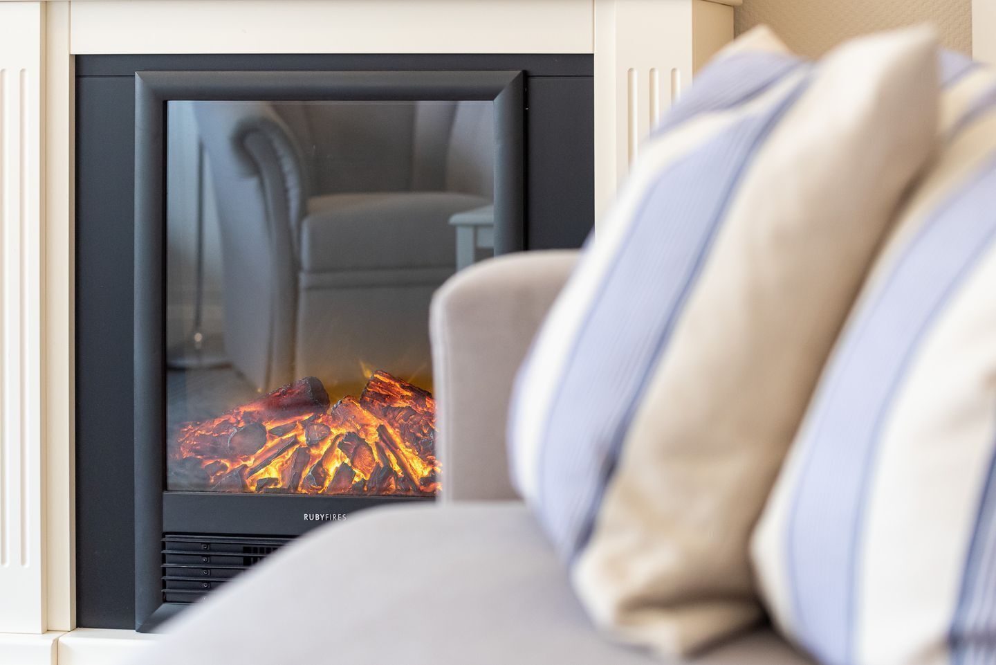 Une cheminée moderne avec une façade en verre, un canapé avec des coussins à rayures et un feu visible qui brûle à l’intérieur.