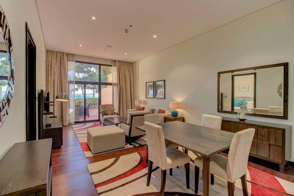 A modern hotel room with a dining area, a large mirror, and a view of the outdoors.