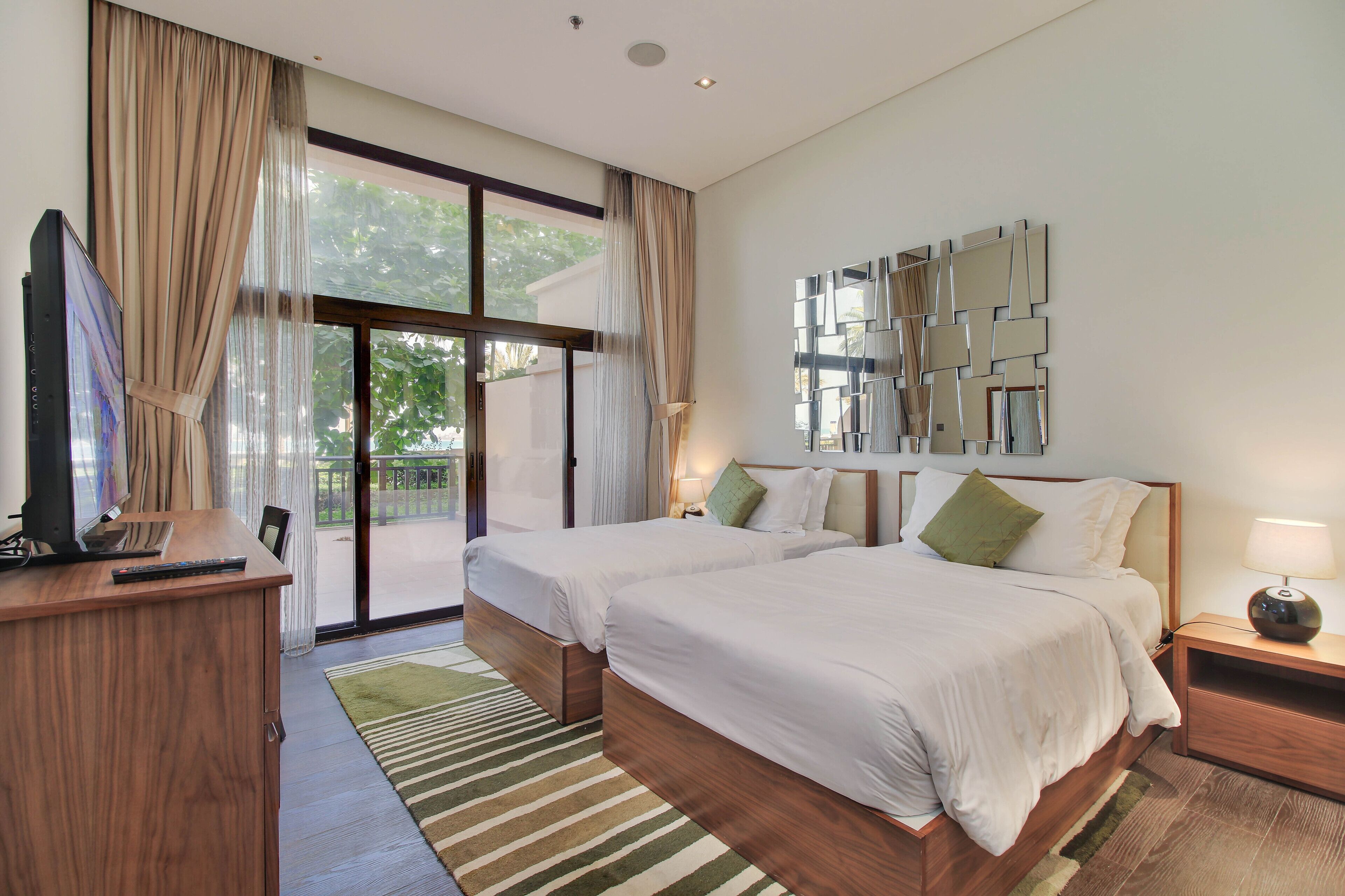A hotel room with two beds, a TV, a desk, and a large window with curtains.
