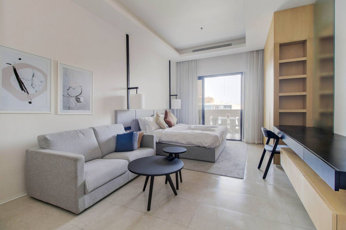 A modern hotel room with a sofa, a small round table, a bed with a view, and a TV.