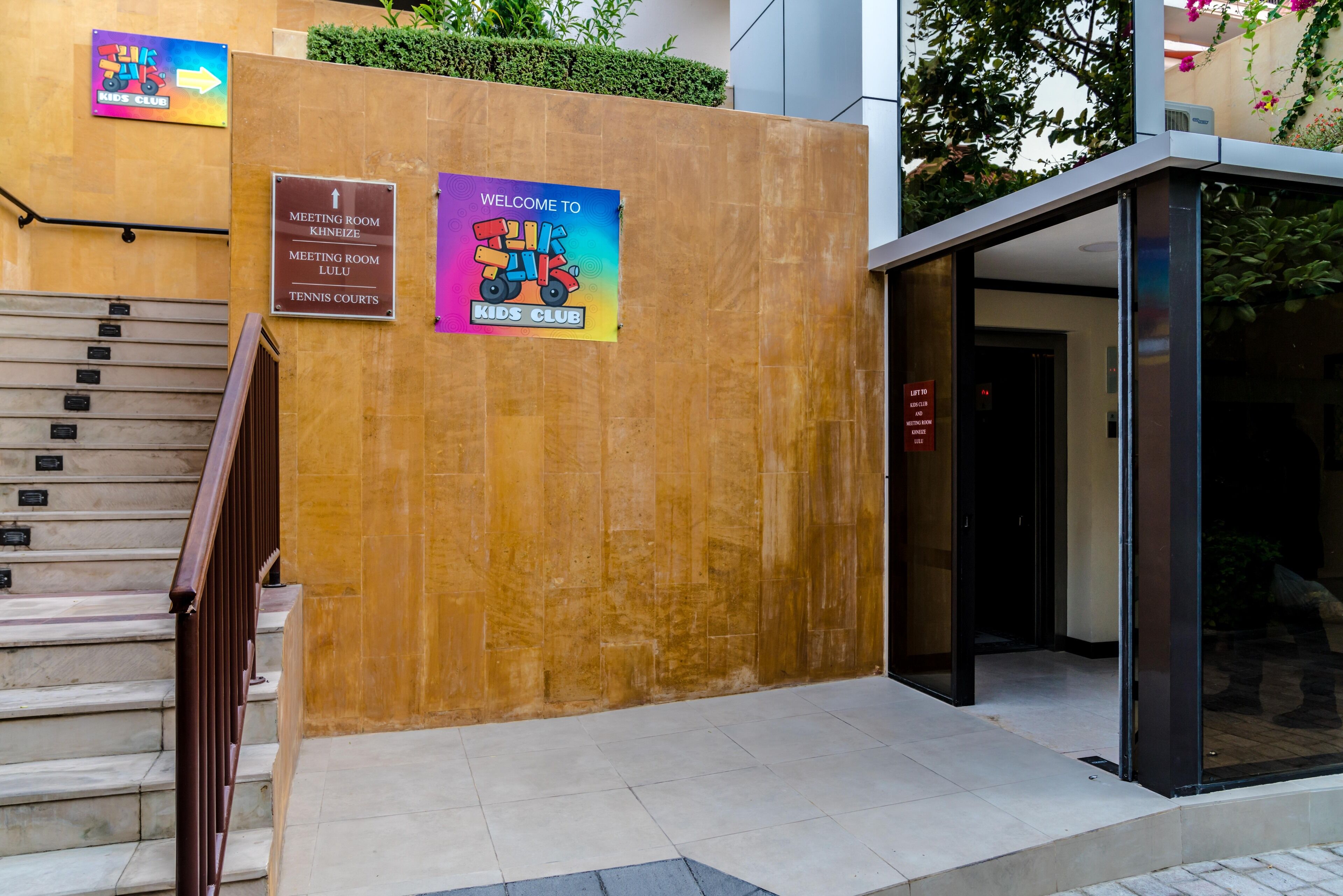 Una entrada de edificio con escaleras, un cartel para el club infantil y un letrero de bienvenida.