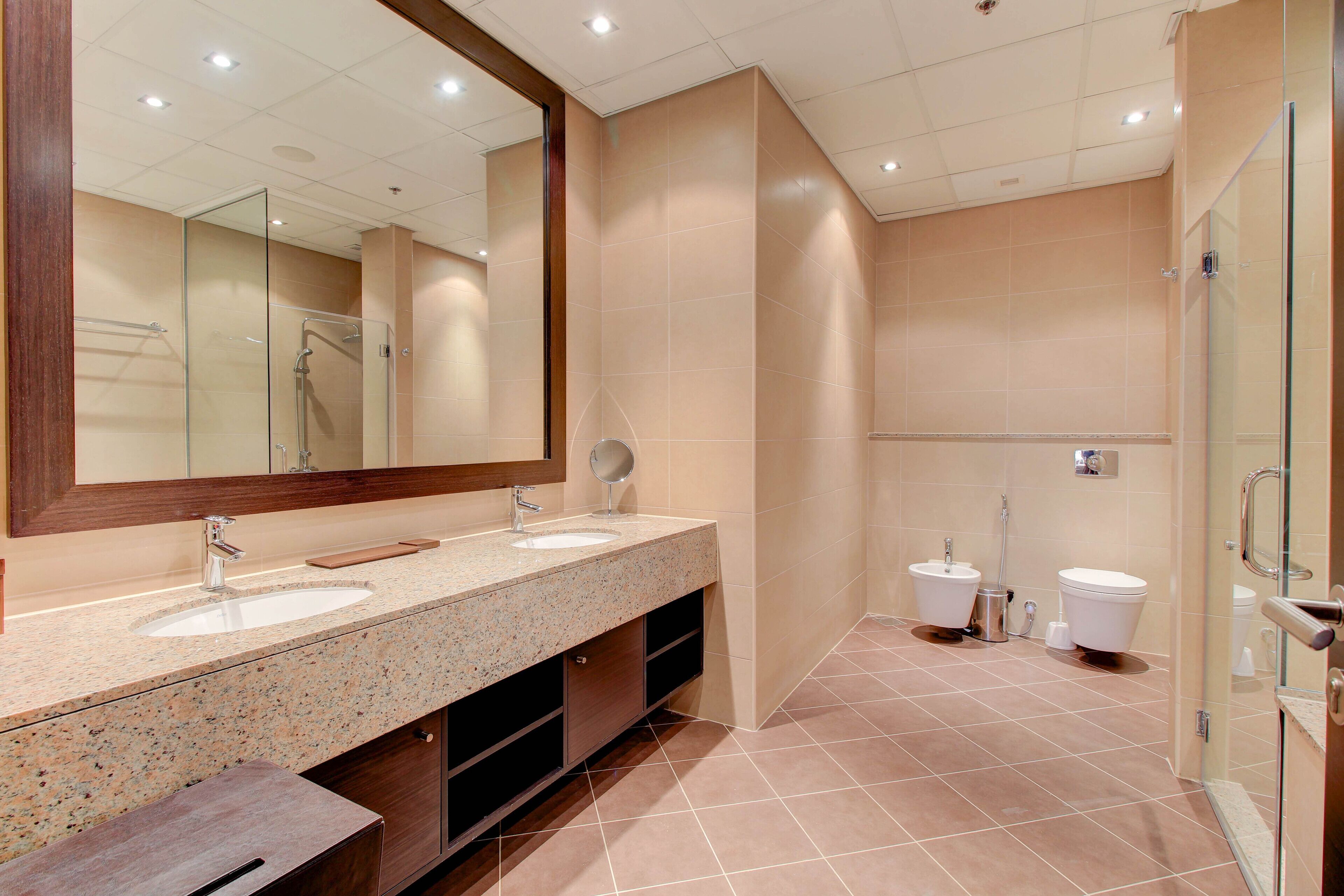 A modern bathroom with two sinks, a large mirror, and a glass shower enclosure.