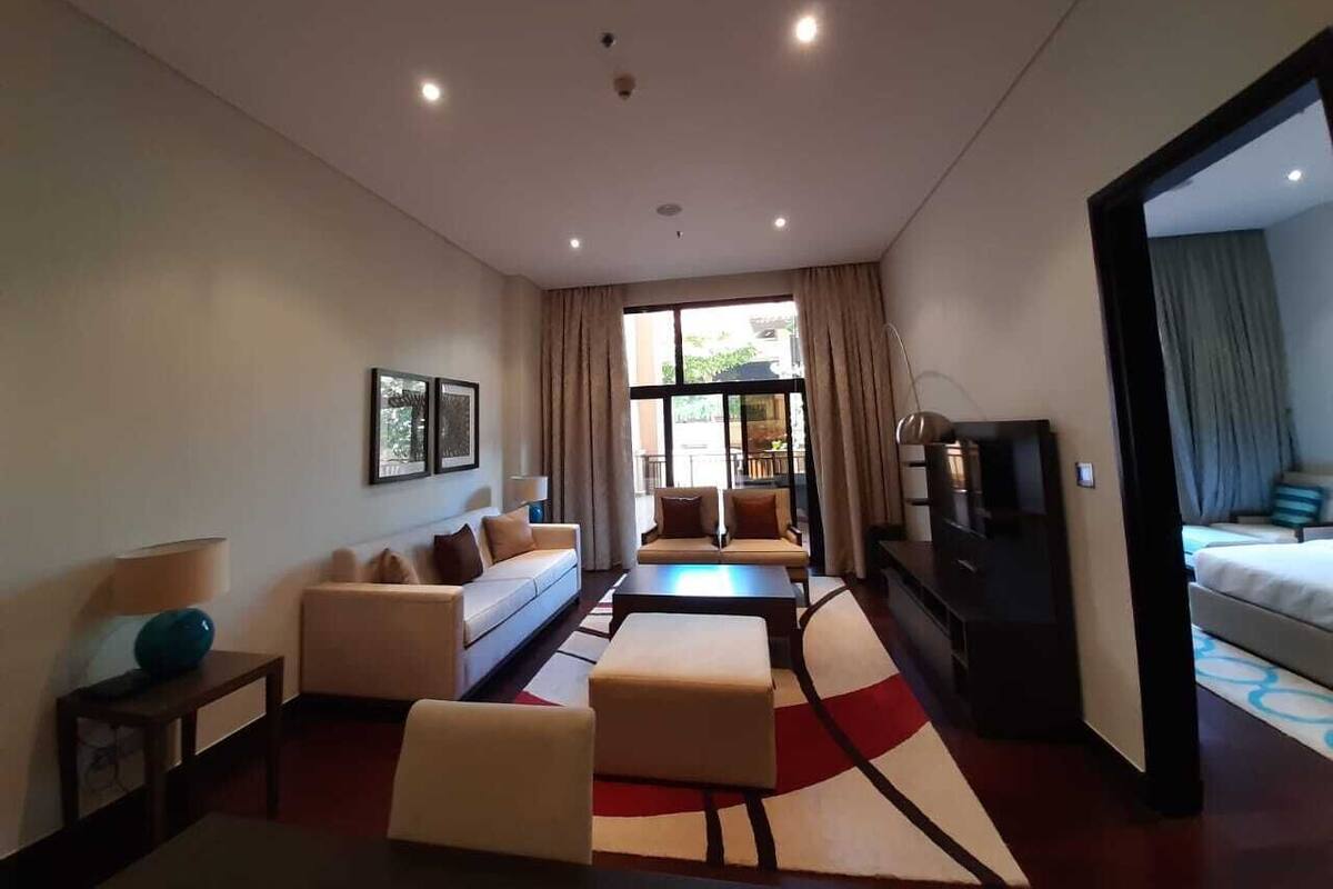 A modern hotel room with a sofa set, a TV, and a large window.