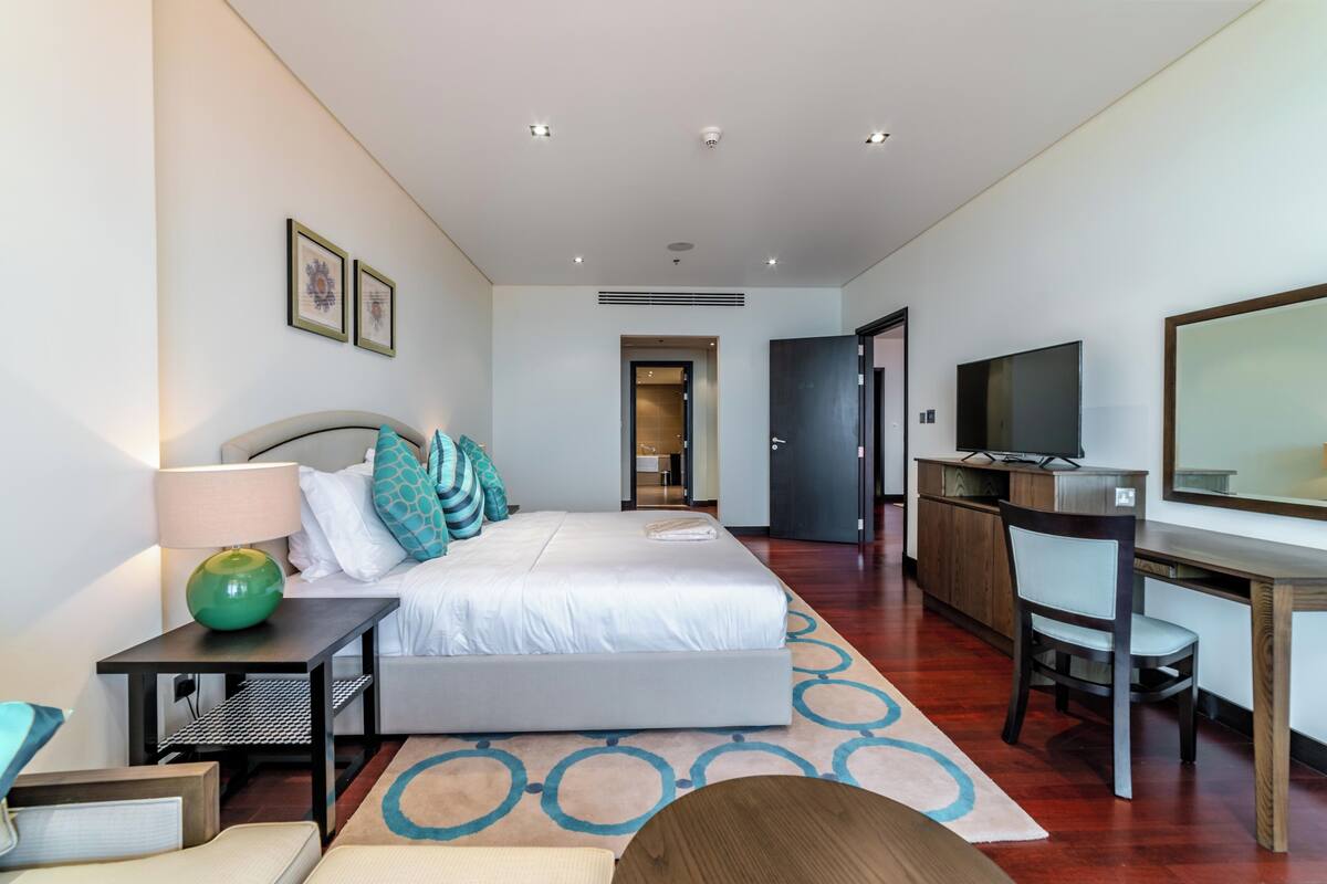 A modern hotel room with a large bed, a desk, a chair, a TV, and a mirror.