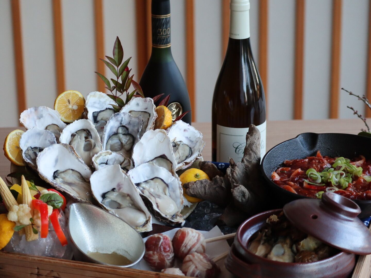 A variety of seafood including oysters, lemon slices, and vegetables, along with a bottle of wine and a pot of stew.