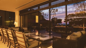 A modern outdoor seating area with a fire feature, comfortable chairs, and large windows offering a view of the sky and trees. - Etajimasou (Etajima)