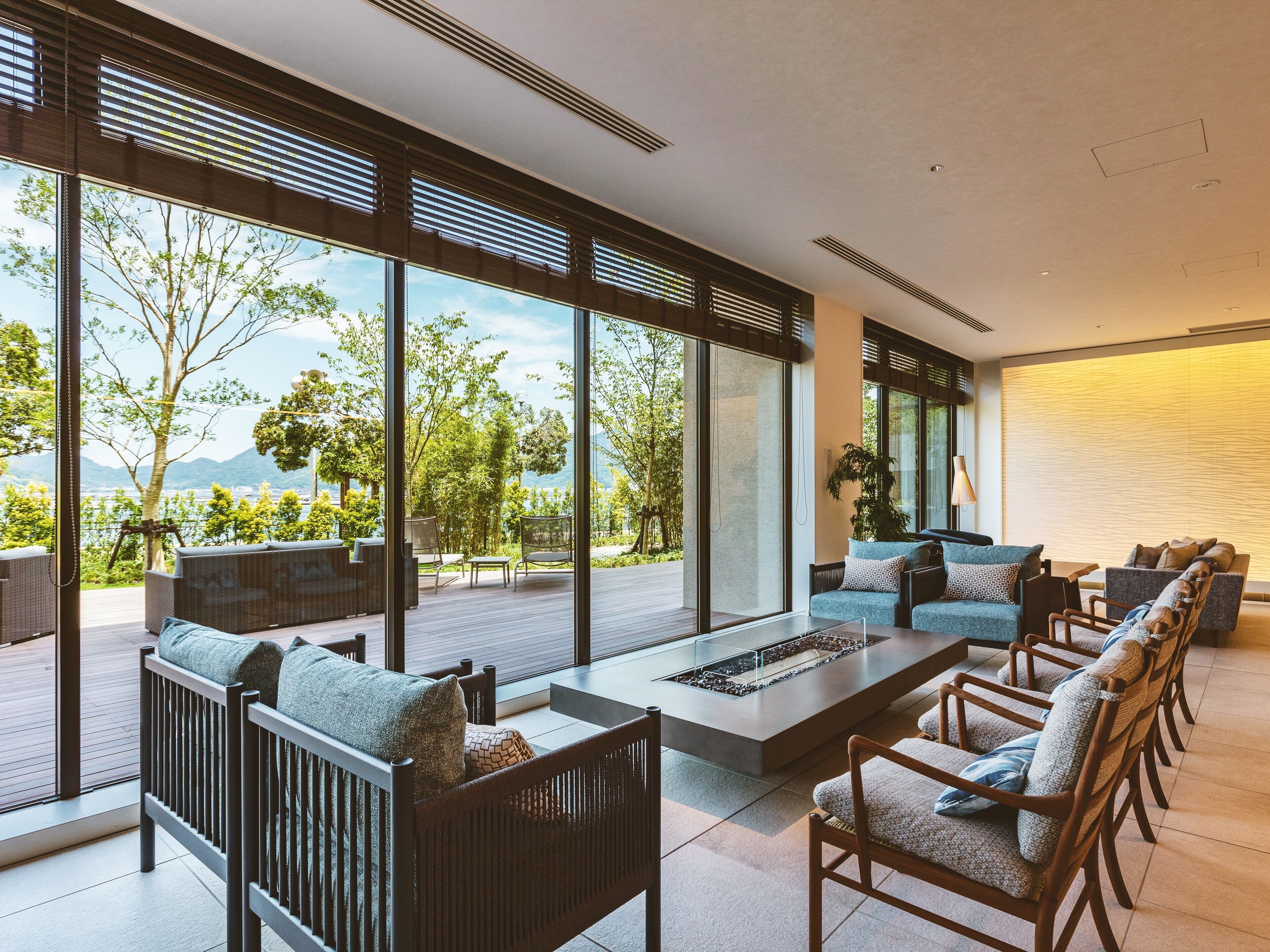 Un espacio de estar moderno al aire libre con una chimenea, ventanas amplias y vistas a zonas verdes y montañas.