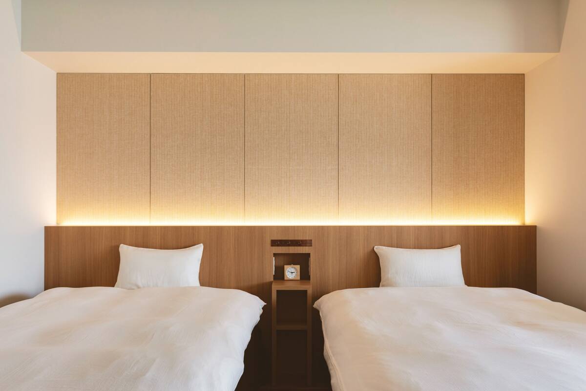 A hotel room with two beds, a wooden headboard, and a nightstand with a clock.