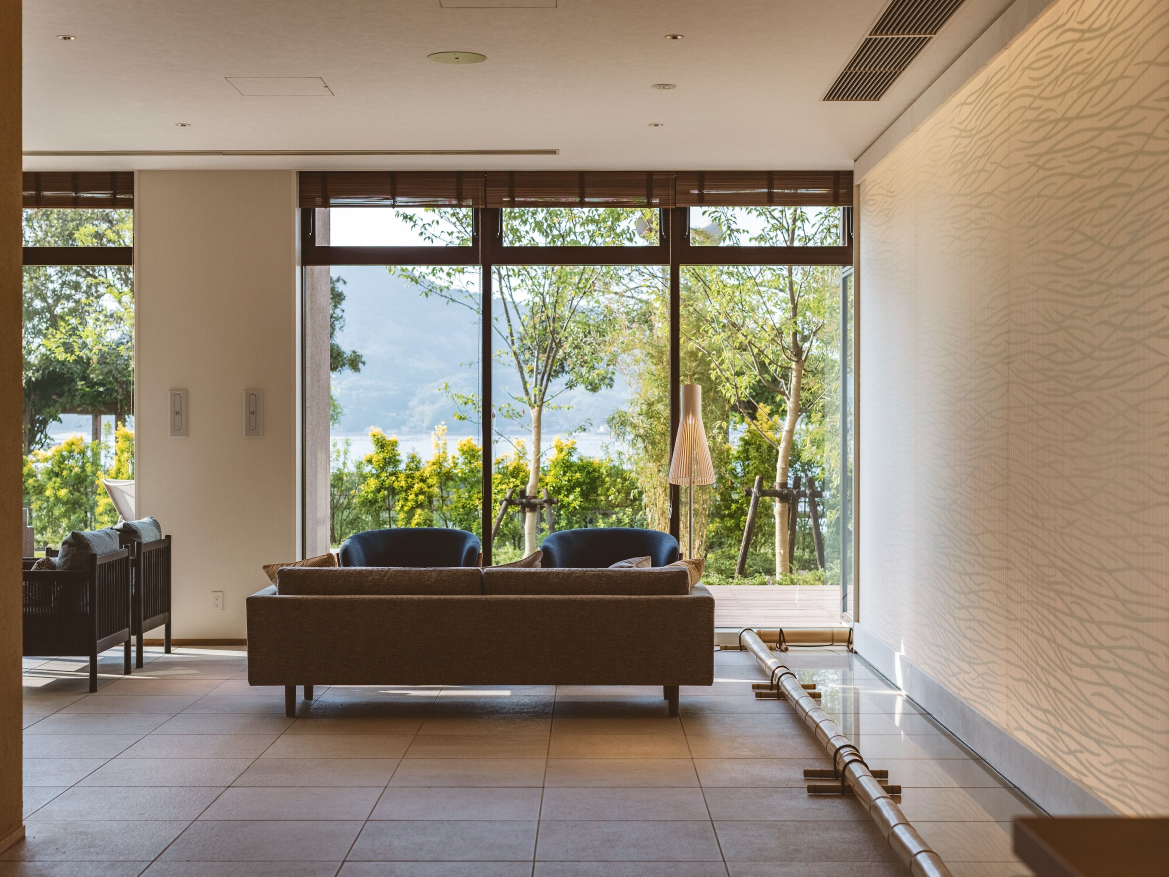 Habitación moderna con sofá, una silla y un ventanal que ofrece vistas a árboles y una masa de agua.