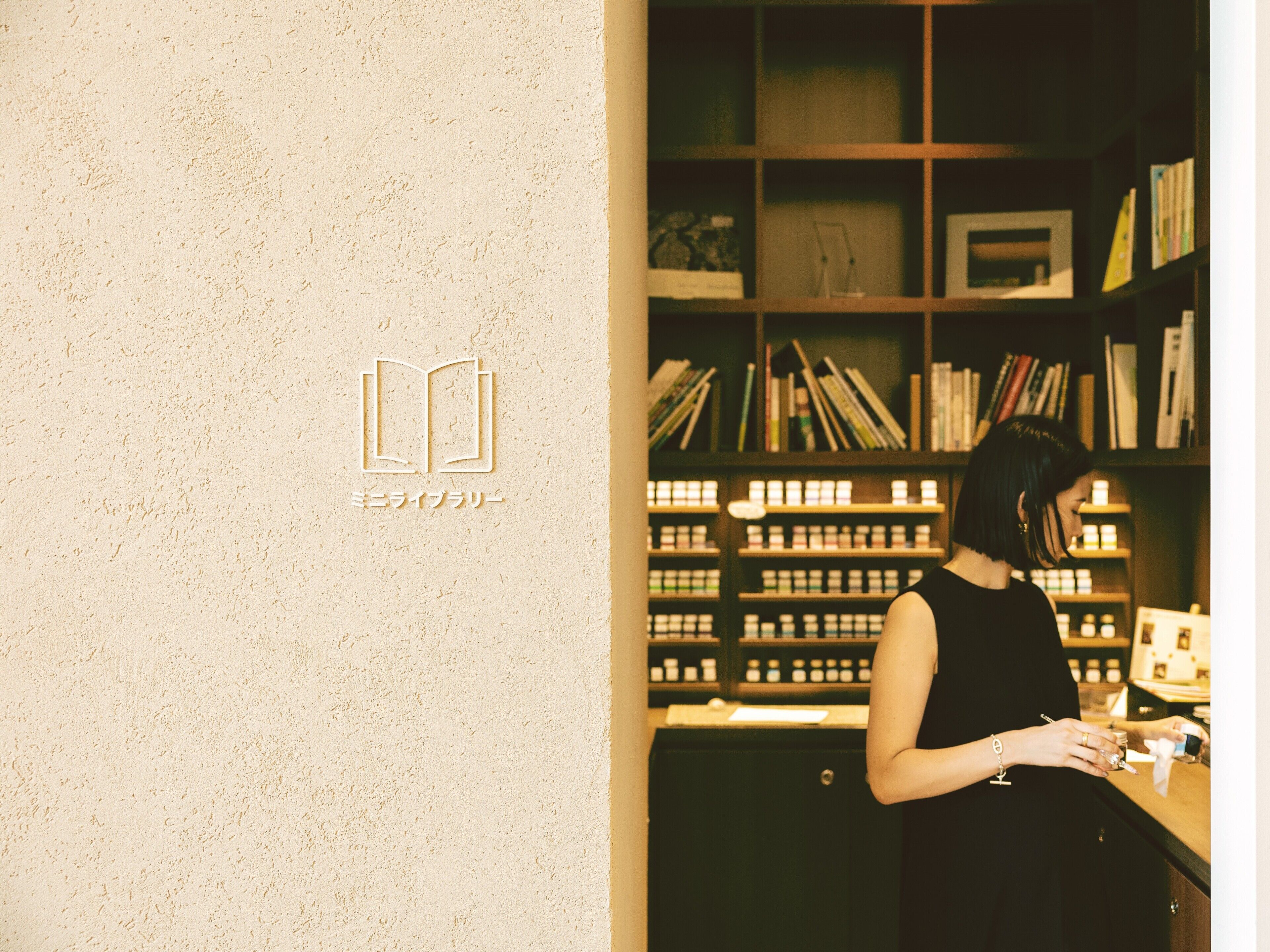 A person standing at a counter with a bookshelf in the background.