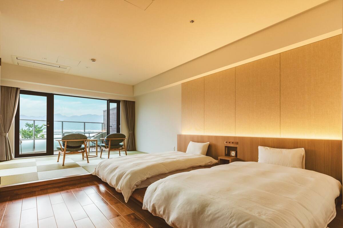 A hotel room with two beds, a balcony with a view, a small table, and chairs.