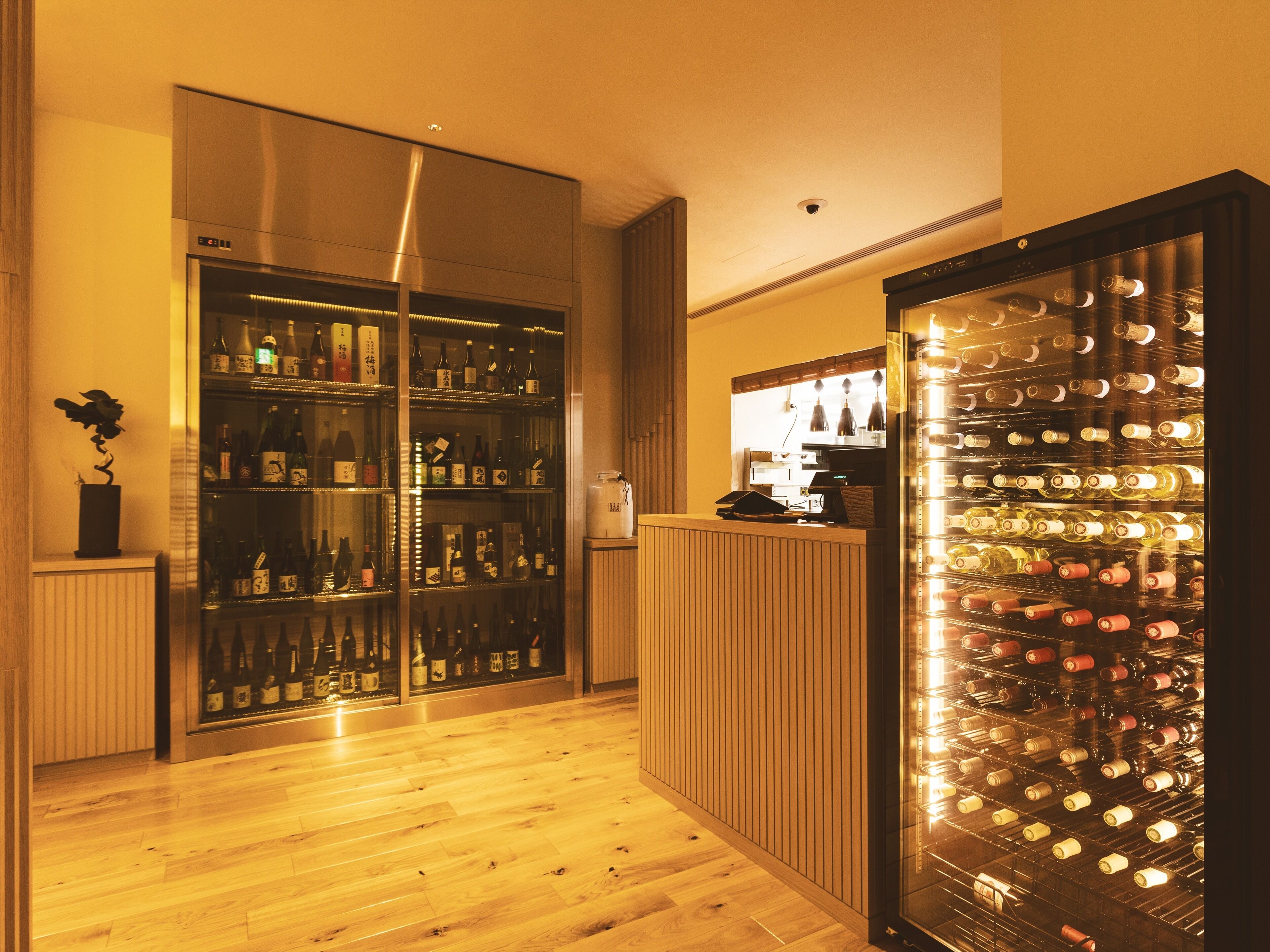A bar area with shelves of bottles, a wine cooler, and a wooden counter.