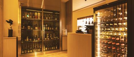 A bar area with shelves of bottles, a wine cooler, and a wooden counter.