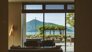 A room with a large window overlooking a scenic view of a mountain and a body of water. There is a sofa and two chairs in the foreground. - Etajimasou (Etajima)