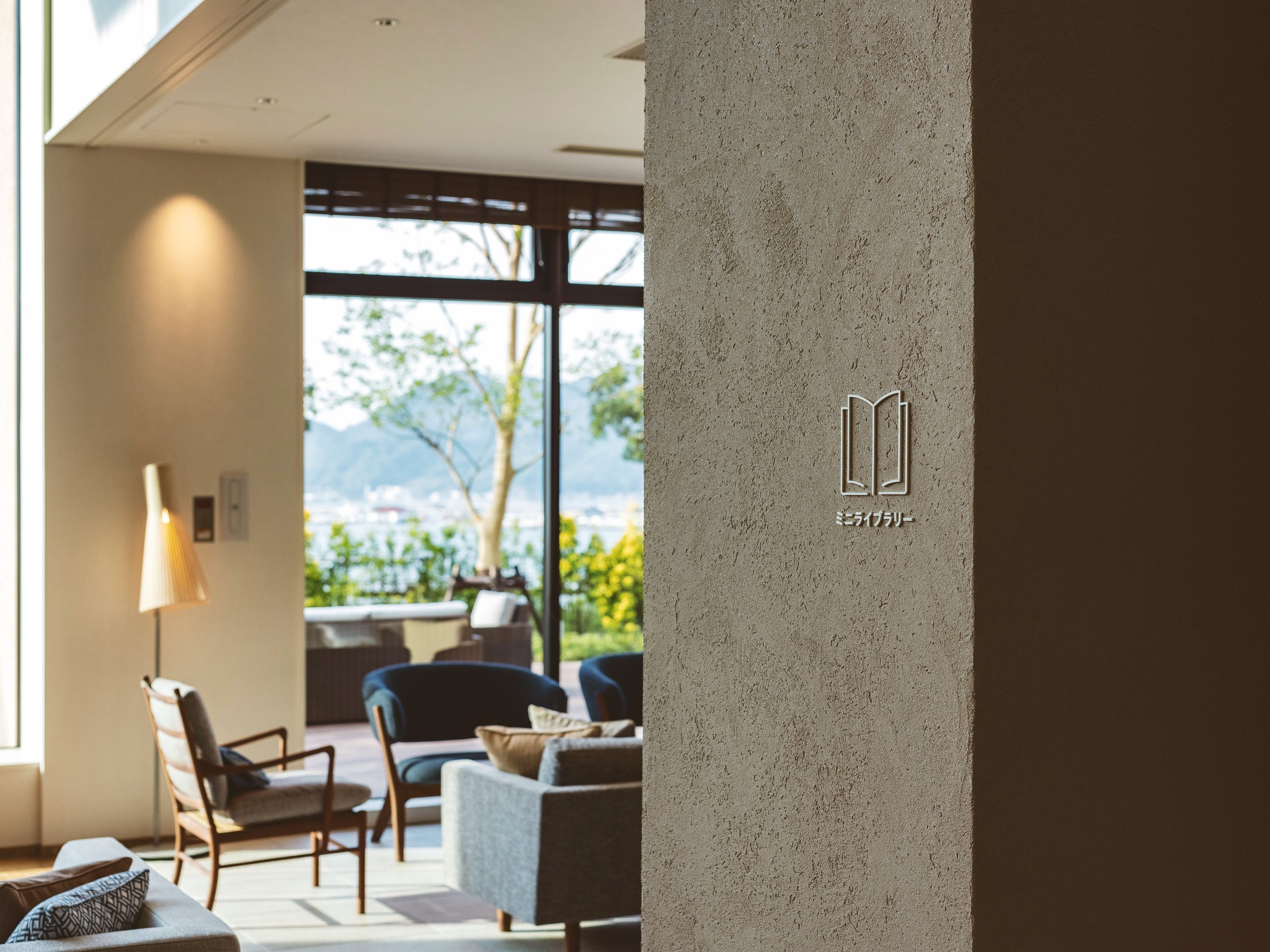 Ein modernes Interieur mit einer Couch, Sesseln und einer Lampe. Ein großes Fenster bietet Blick auf Grünflächen und Berge.