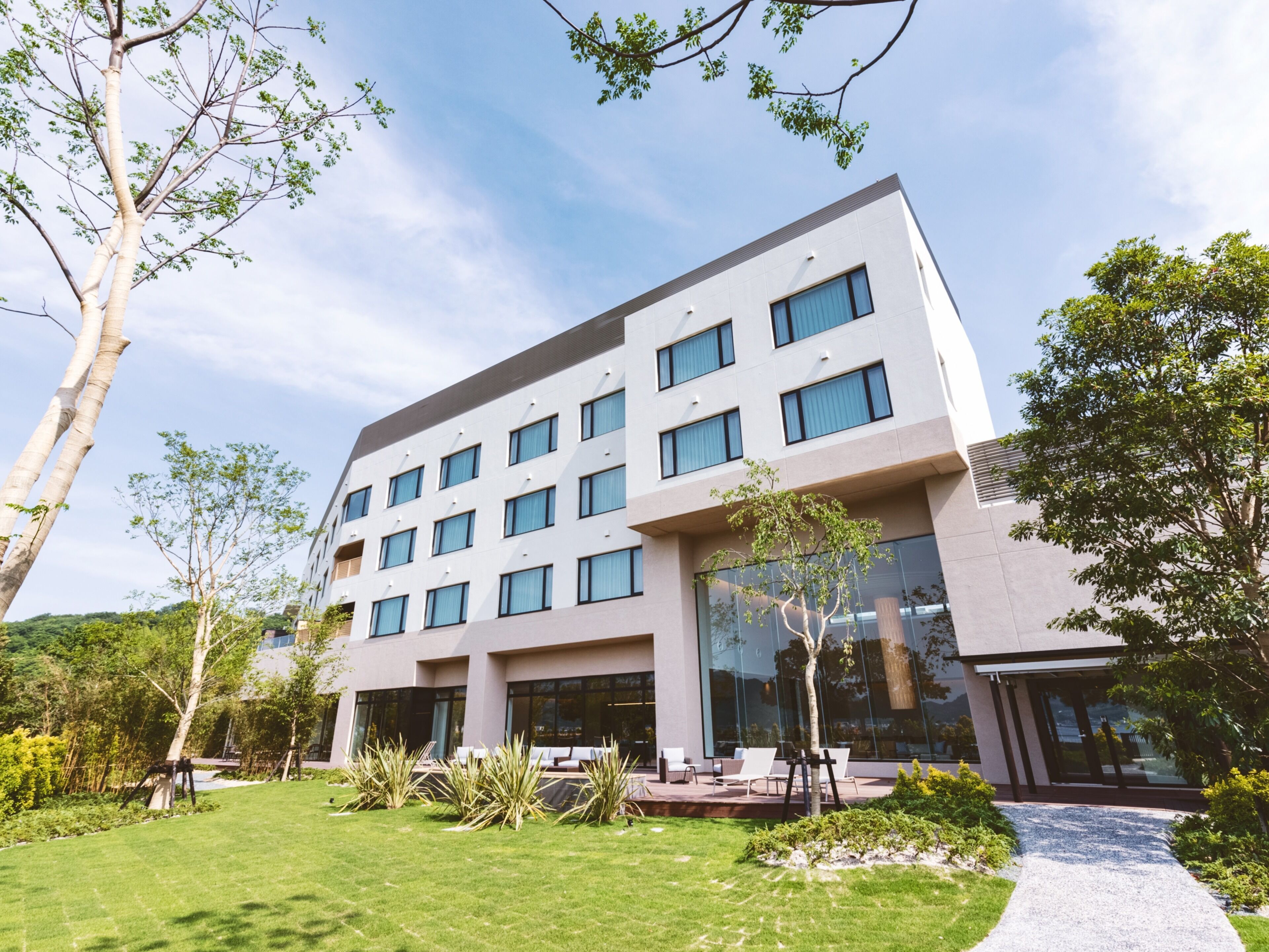 Un hotel moderno con techo plano, numerosas ventanas y un césped cuidado con mobiliario de exterior.