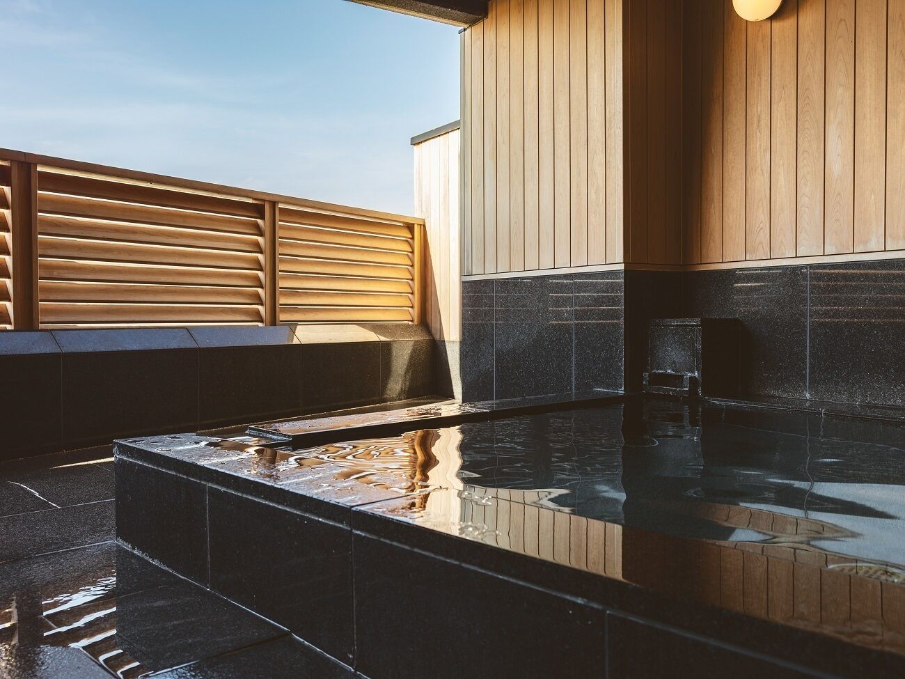 A modern outdoor hot tub area with a wooden deck and a stone-tiled floor.