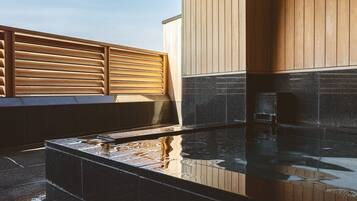 A modern outdoor hot tub area with a wooden deck and a stone-tiled floor.