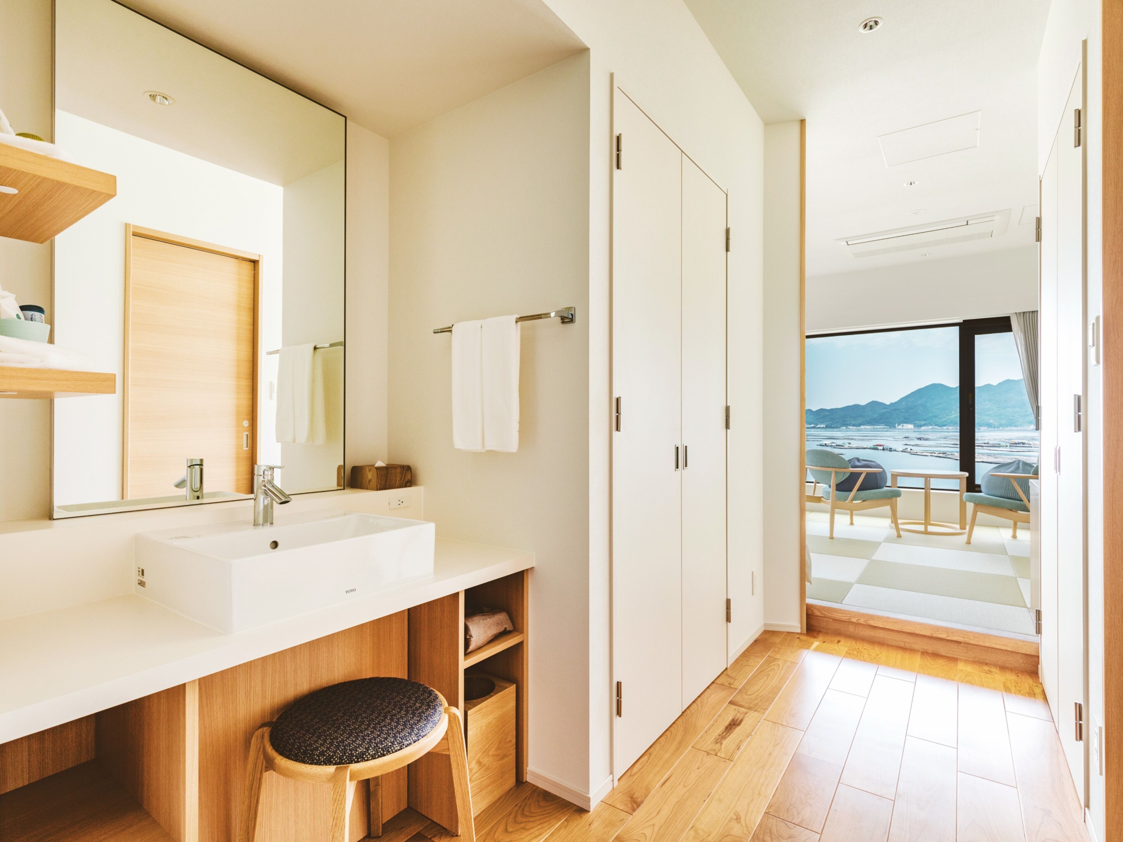 A modern bathroom with a large mirror, a sink, and a wooden chair.