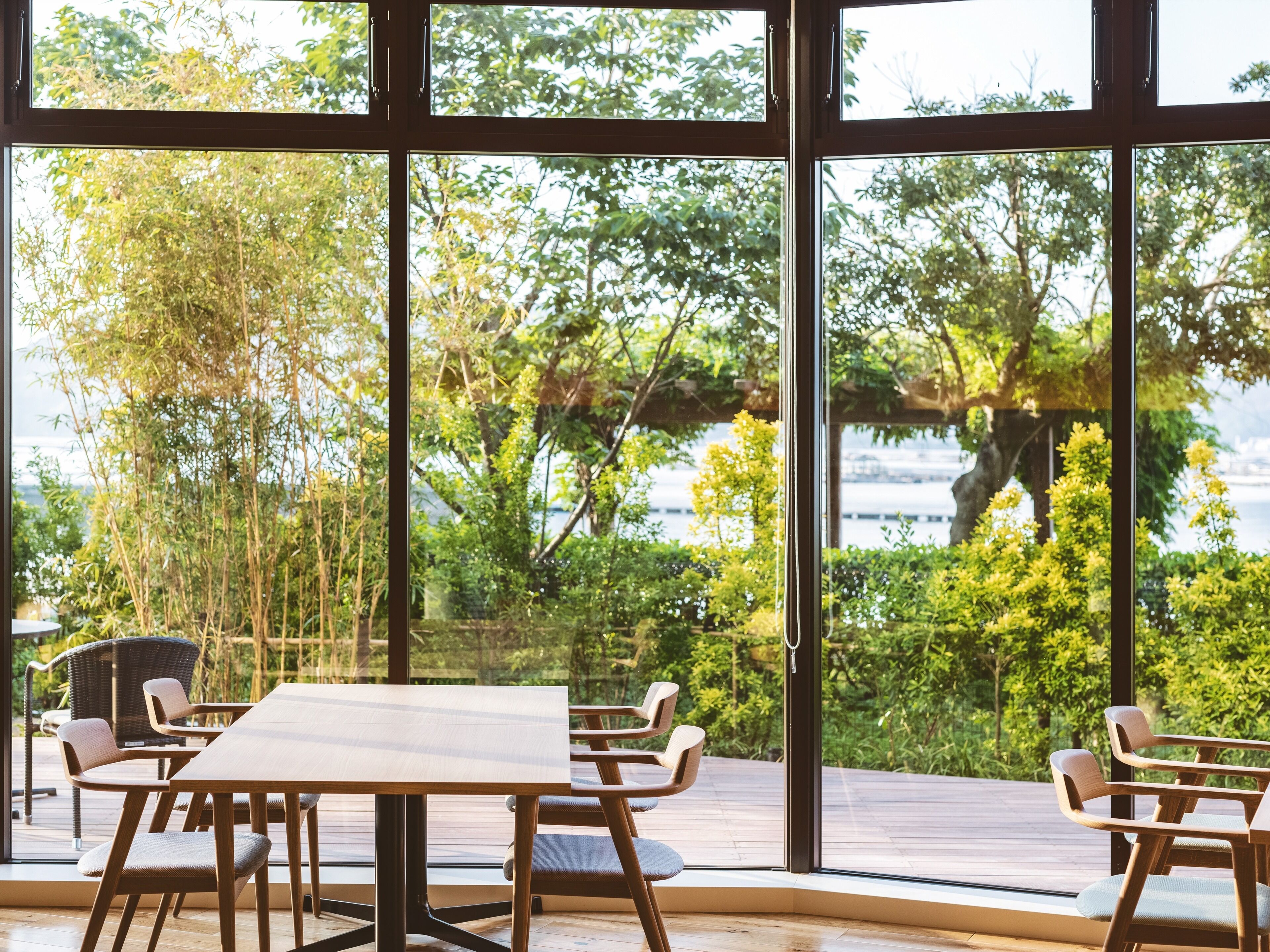 Un comedor con mesa y sillas, ventanas amplias y vistas a follaje y una masa de agua.