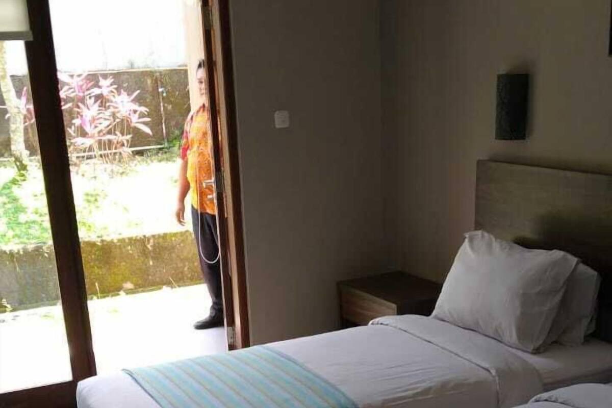 Ein Hotelzimmer mit zwei Betten, einem Nachttisch und einer Glastür, die zu einem Außenbereich führt.