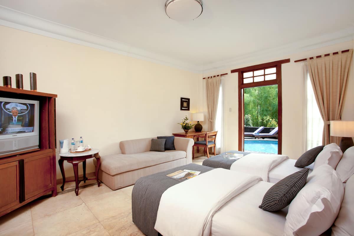 Ein Hotelzimmer mit Bett, Fernseher, Schreibtisch, Stuhl und Blick auf einen Pool.