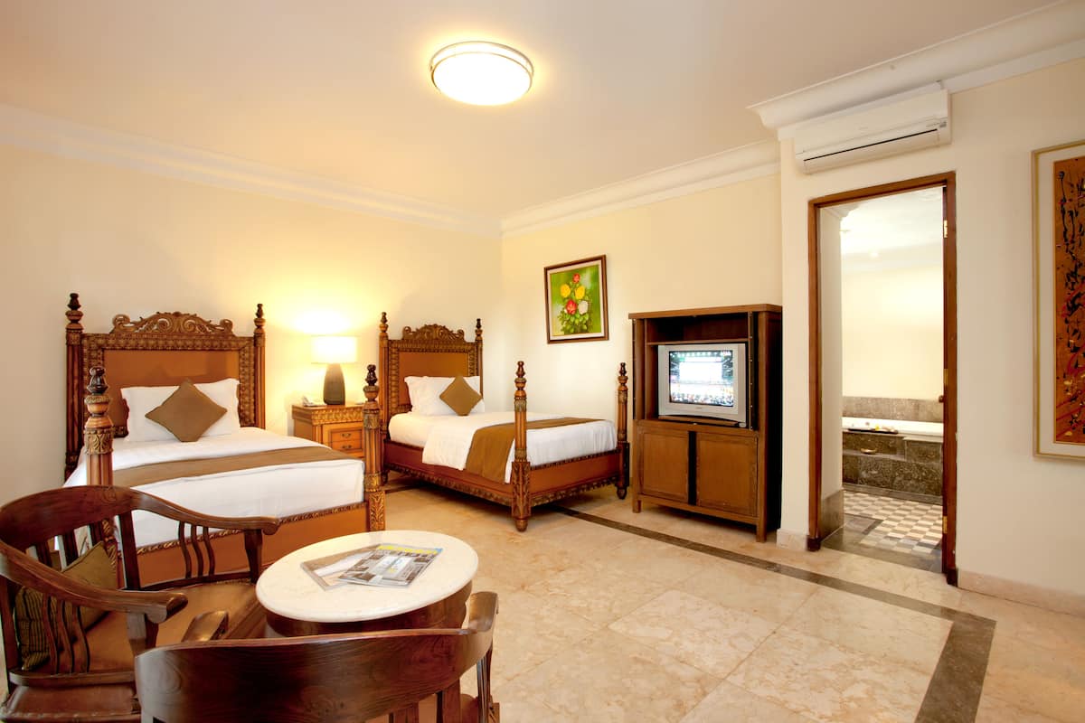 Ein Hotelzimmer mit zwei Holzbett, einem Fernseher, einem Tisch mit Stühlen und einem durch eine offene Tür einsehbaren Badezimmer.