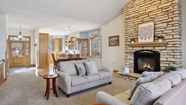 A cozy living room with a stone fireplace, a dining area, and a kitchen in the background.