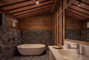 A bathroom with a freestanding bathtub, a sink with a mirror, and a stone-tiled shower area. - RUMAH KAYU RESORT (Ubud)
