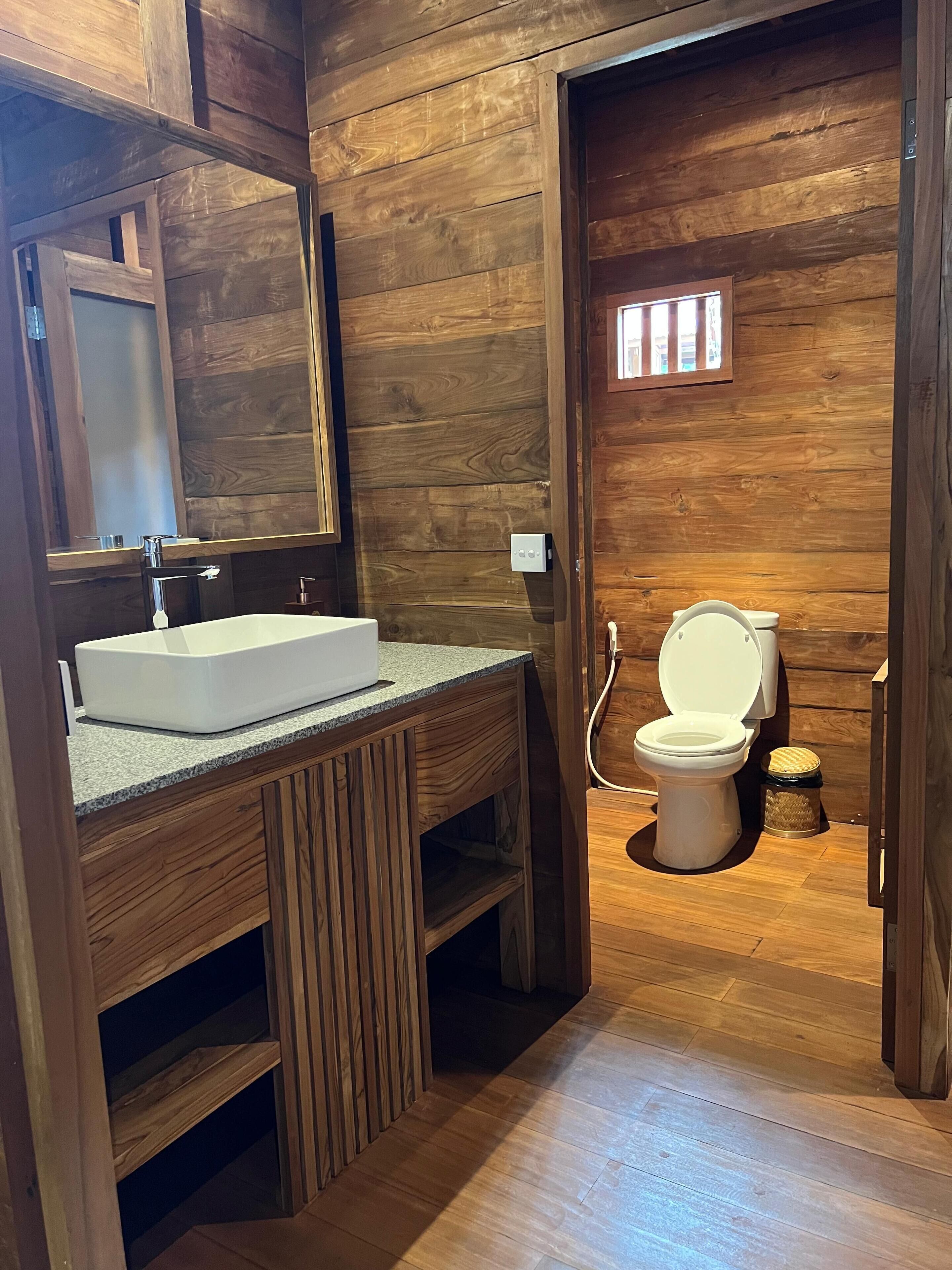 Un baño de madera con un lavamanos, espejo y retrete blancos.