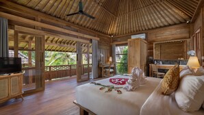 A spacious room with a large bed, a desk, and a television. - RUMAH KAYU RESORT (Ubud)