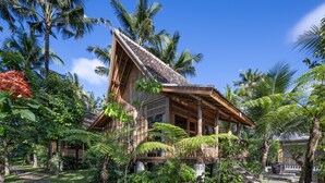 A tropical resort with a thatched roof, surrounded by lush greenery and palm trees. - RUMAH KAYU RESORT (Ubud)