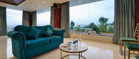 Un salón amplio con un sofá azul aguamarina, una mesa de centro redonda y vistas al exterior a través de ventanas grandes.