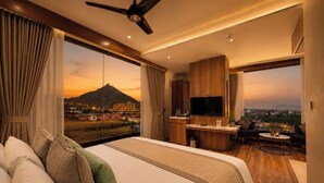 Ein Hotelzimmer mit Bett, Fernseher, Schreibtisch und Blick auf einen Berg bei Sonnenuntergang.