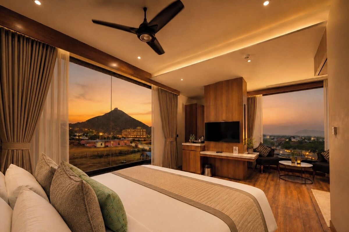 Une chambre d’hôtel avec un lit, une télévision, un bureau et une vue sur une montagne au coucher du soleil.