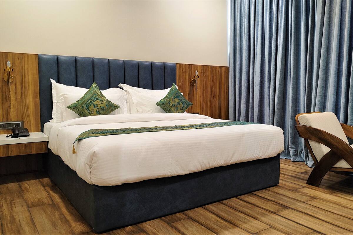A modern hotel room with a large bed, two decorative pillows, a bedside phone, and a wooden nightstand.
