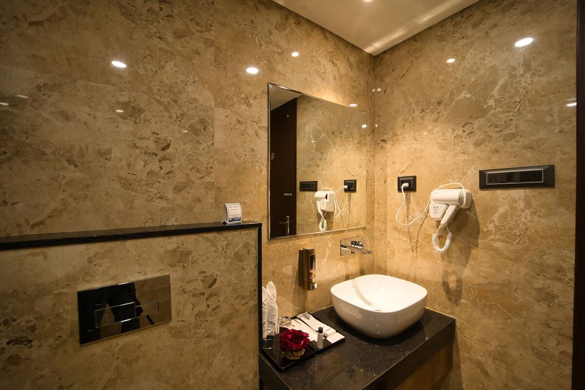 A modern bathroom with a marble wall, a large mirror, a sink, a hairdryer, and a towel dispenser.