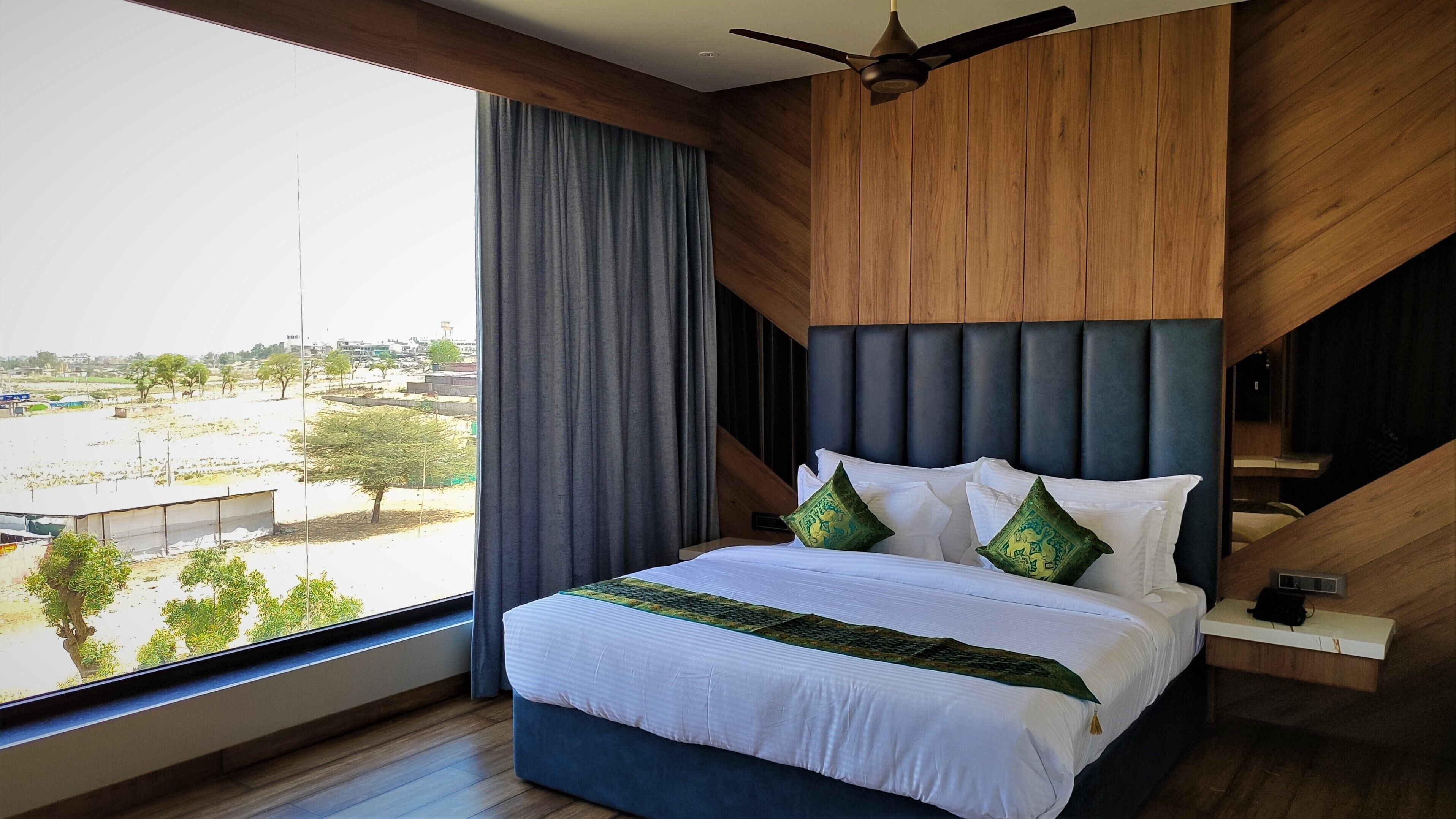 A modern bedroom with a large bed, a ceiling fan, and a view of a cityscape.