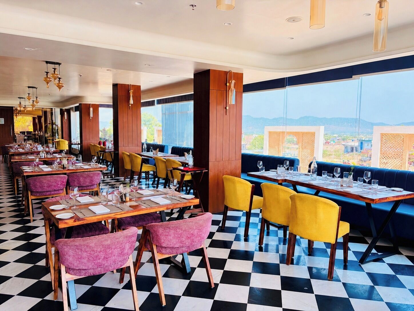 A restaurant with checkered flooring, yellow and purple chairs, wooden tables, and large windows offering a view.