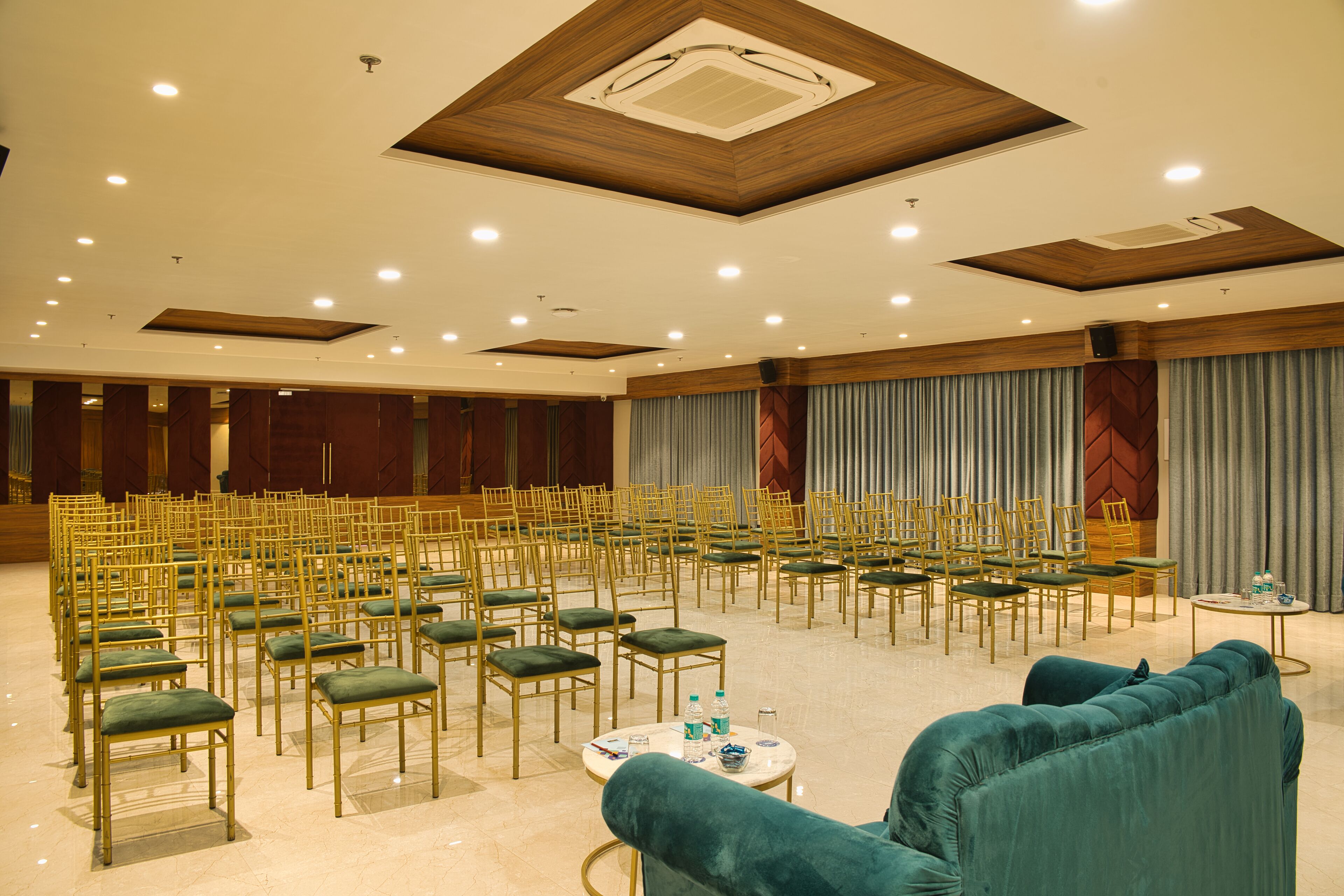 Une salle de conférence avec des rangées de chaises, une table ronde avec des bouteilles d’eau et un canapé vert.